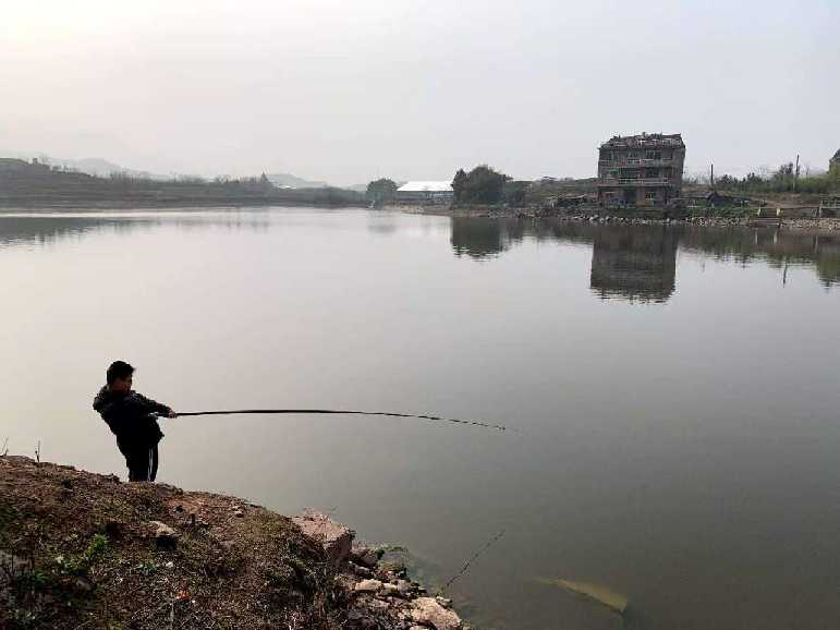 A child fishing from a dirt bank on a still lake