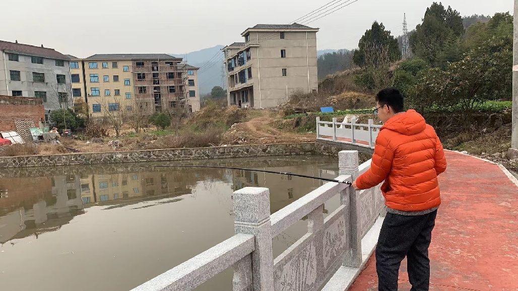Tianqiqi in an orange jacket fishing from a stone bridge